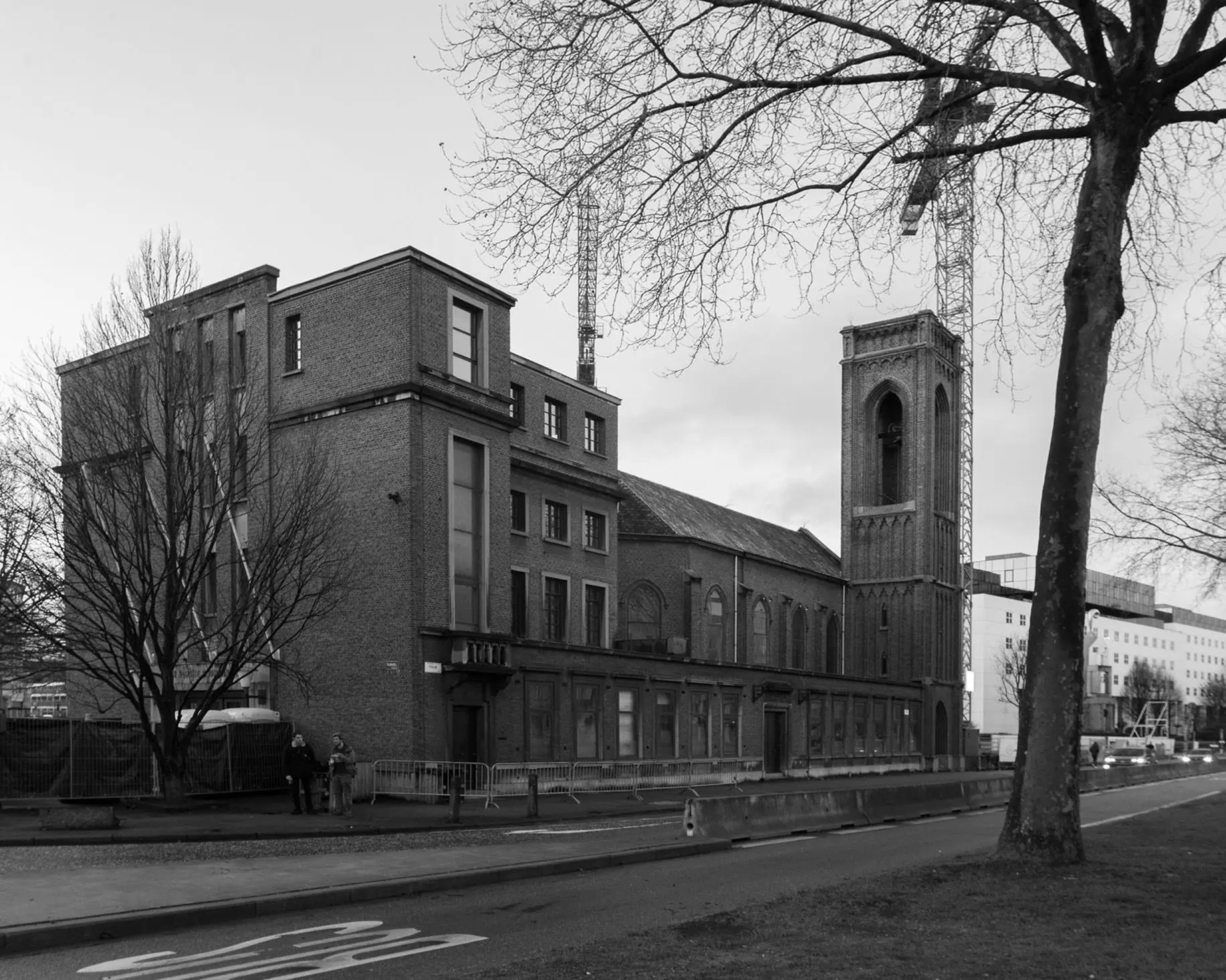 Black-and-white brick building with square tower, bare tree, and construction crane behind.