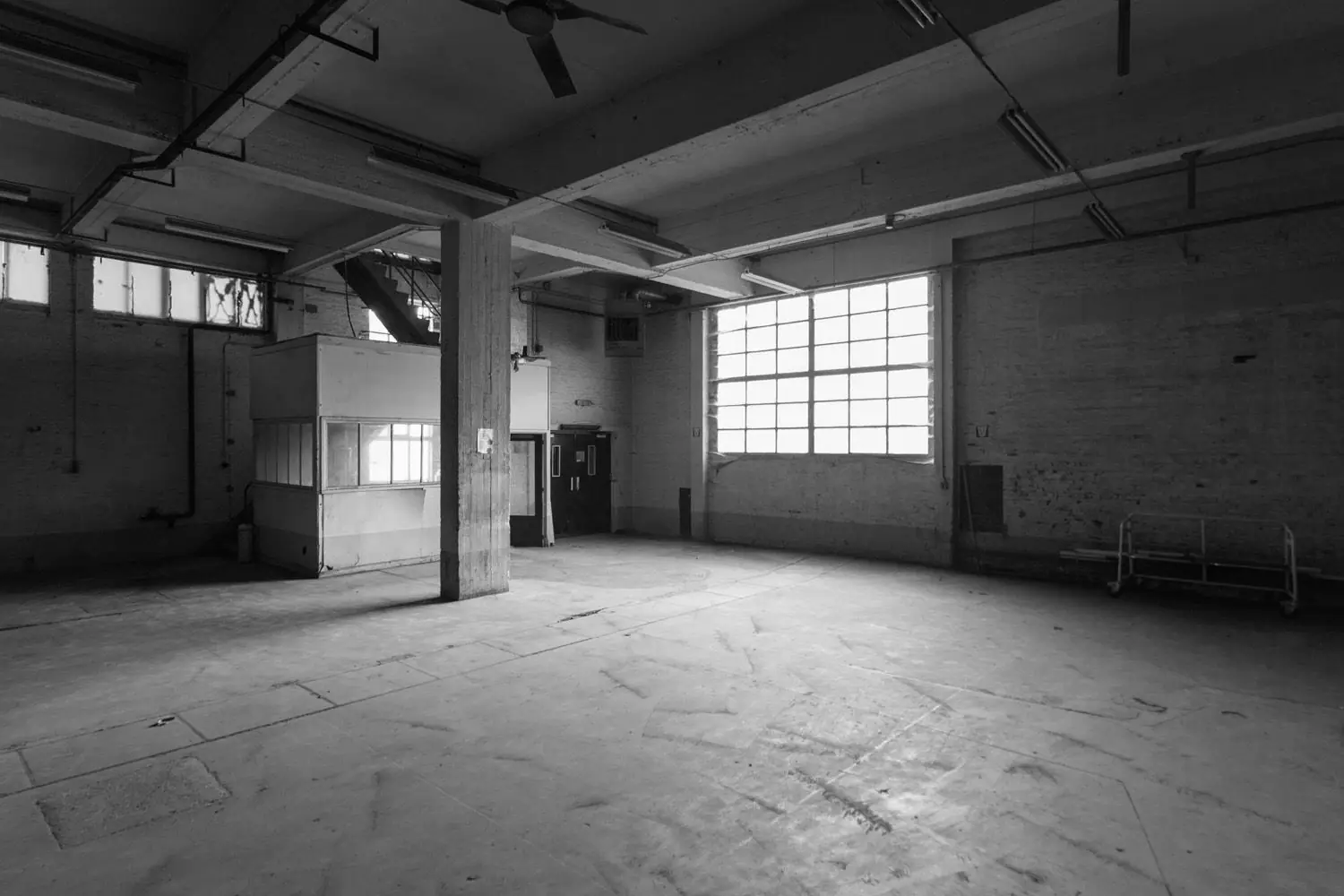 Empty warehouse interior with concrete floor, pillar, small office booth, and large window.