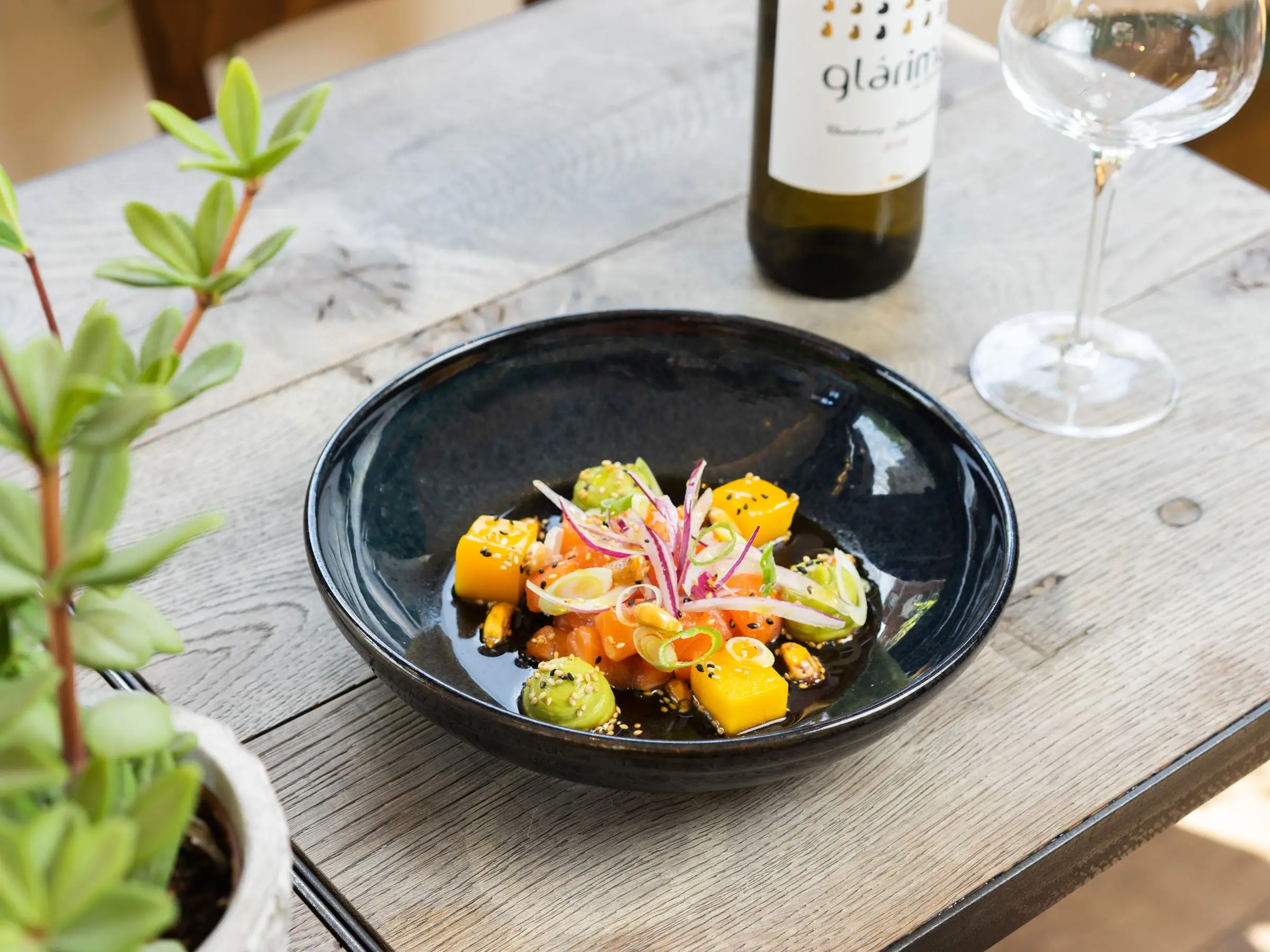 Salmon nikkei bowl with mango, avocado, onion and sesame on a wooden table.
