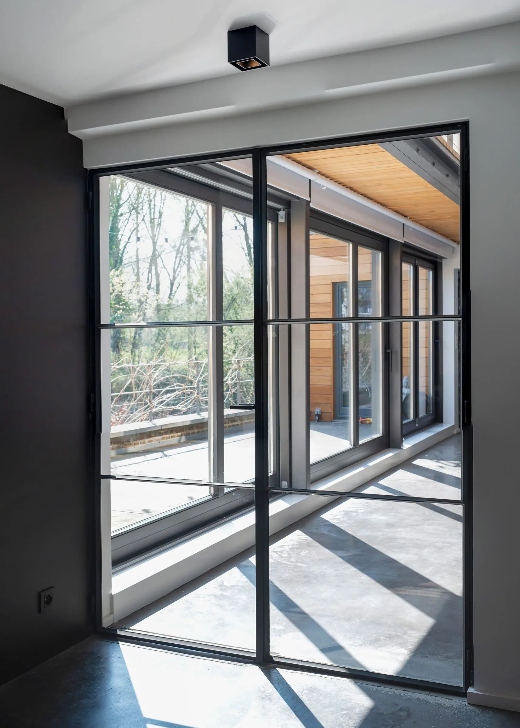 Black-framed glass doors opening onto a sunlit corridor with trees outside.