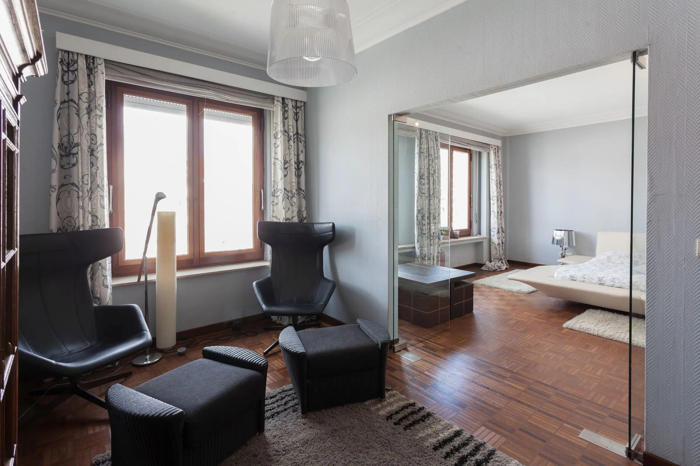 Lounge with black wing chairs and glass partition opening onto a white bedroom.