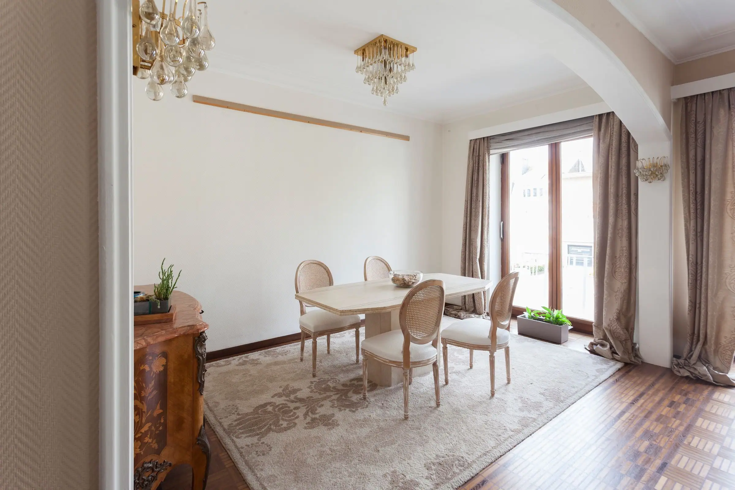 Bright dining room with light wood table, oval-back chairs, and crystal chandelier.