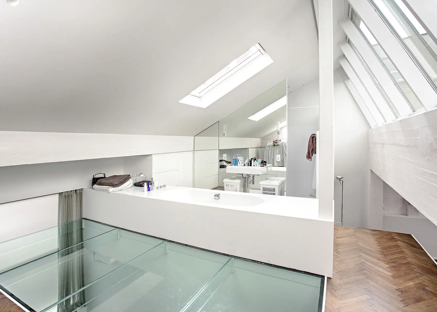 White attic bathroom with oval tub, glass floor panels and sloping skylight.