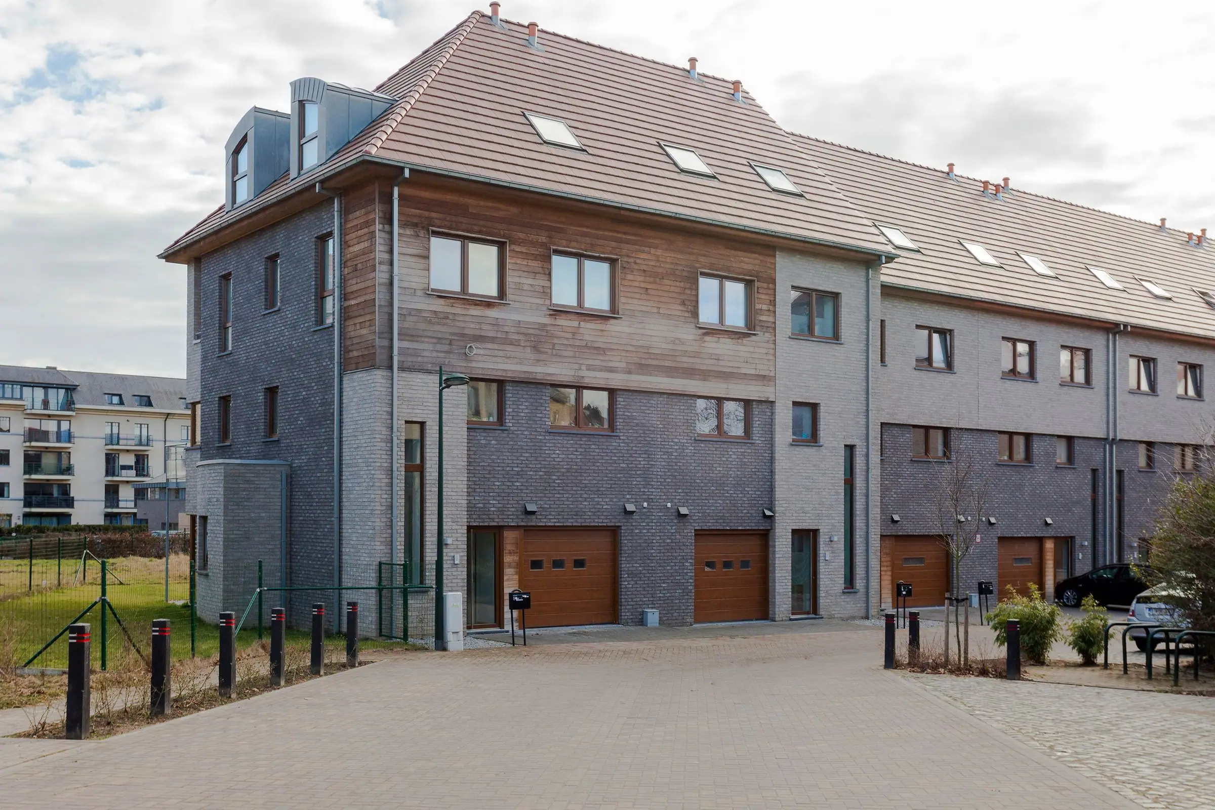 Modern townhouses with grey brick, wood cladding, tiled roof and garage doors.